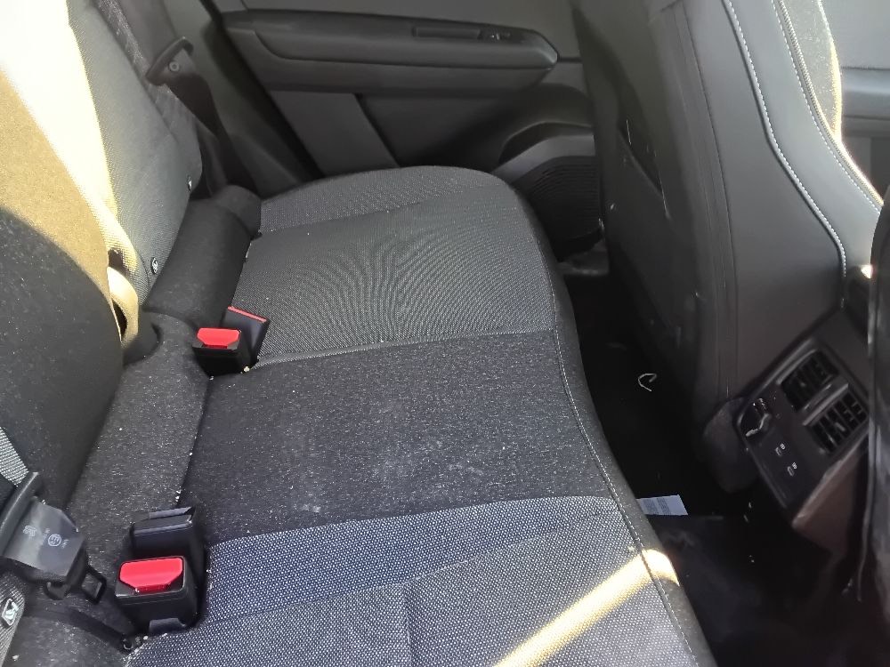 Rear bench seat of the rental car showing a light scatter of crumbs and fine dust on dark cloth upholstery.